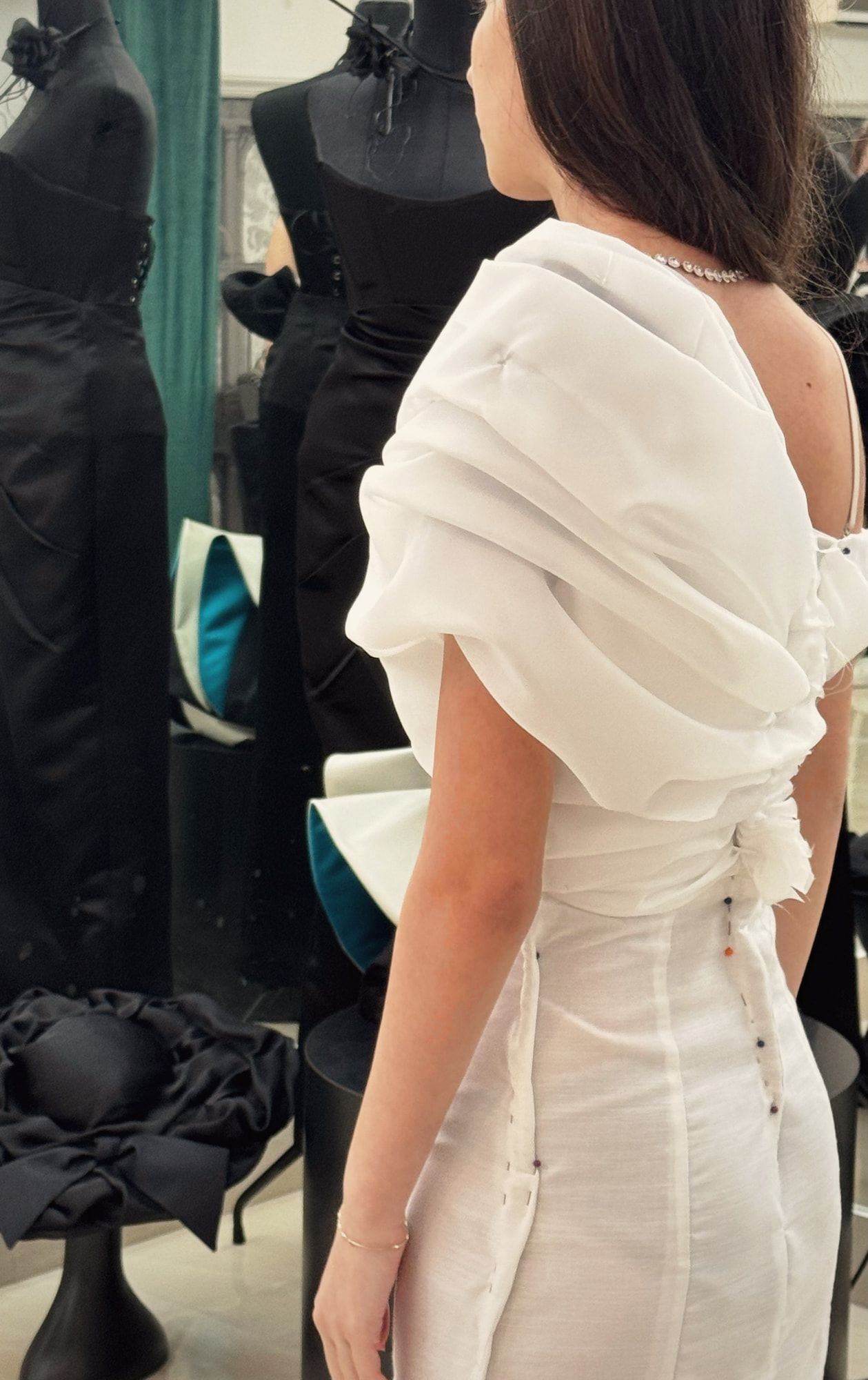Cliente di spalle in abito bianco drappeggiato durante una prova in atelier
