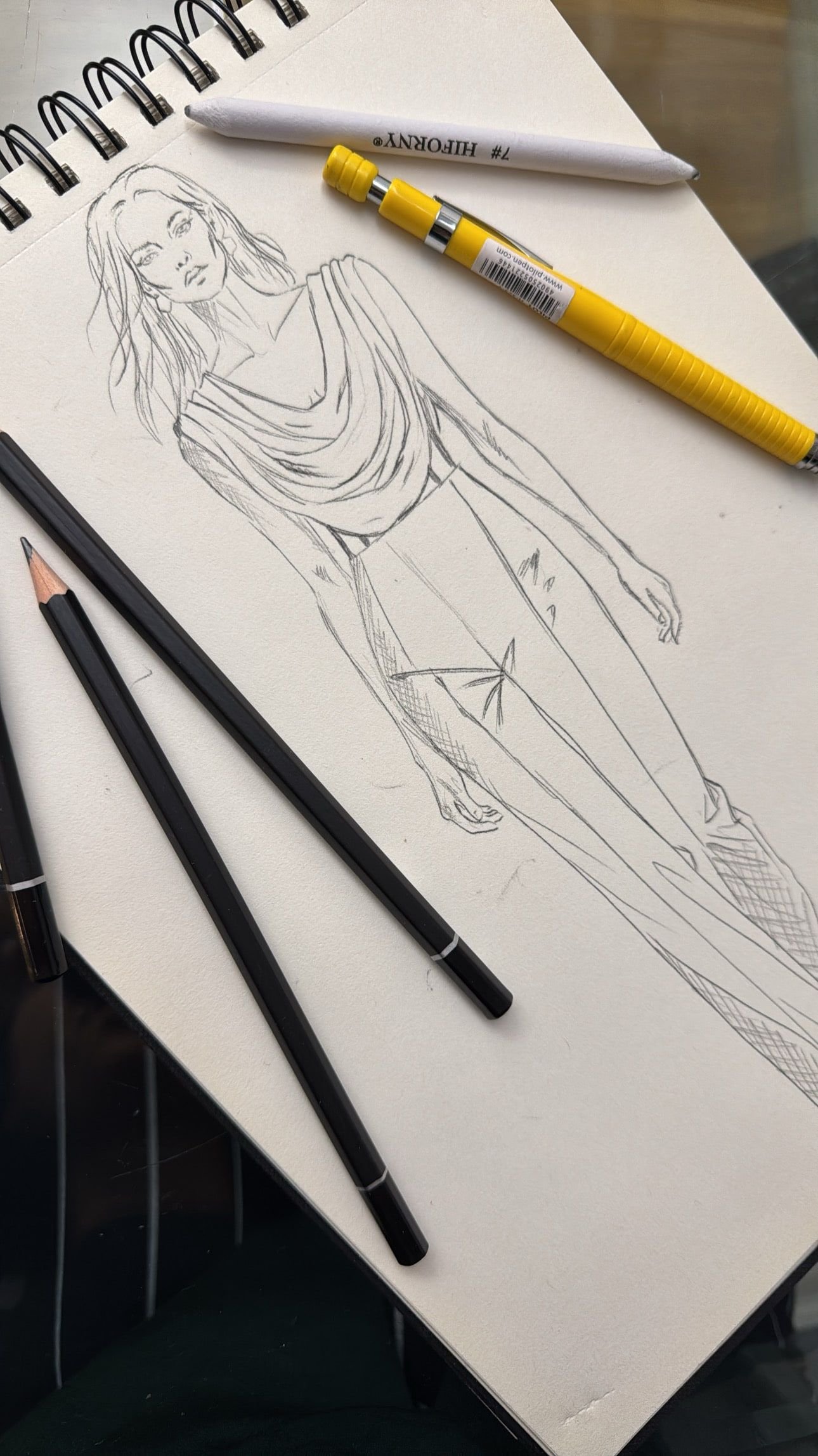 Bozzetto a matita di un abito con drappeggio sul collo, su un blocco da disegno con le matite