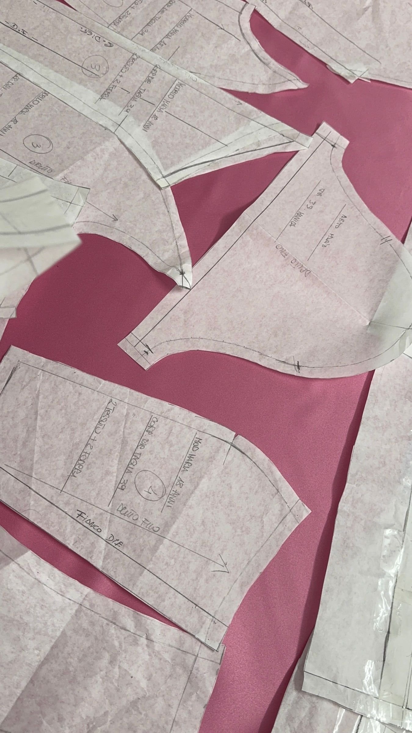 Cartamodelli di carta annotati a mano, appoggiati su un tessuto rosa